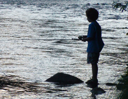 A child fishing from a rock on a shimmering Oregon river at dusk