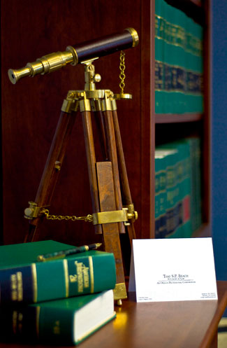 Brass telescope on a wooden tripod beside the firm's card and law books